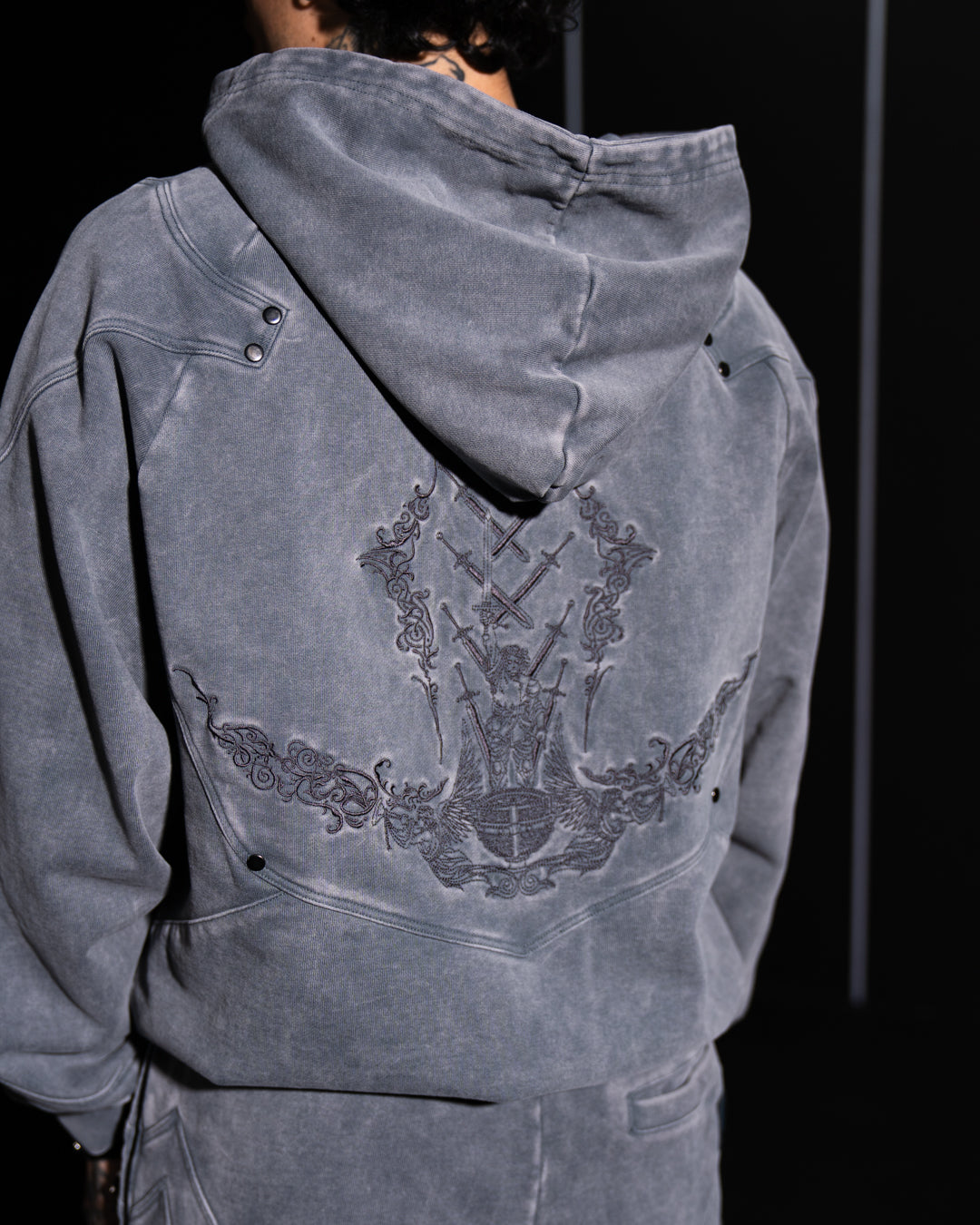 Gray hoodie with embroidery design on the back against a dark background