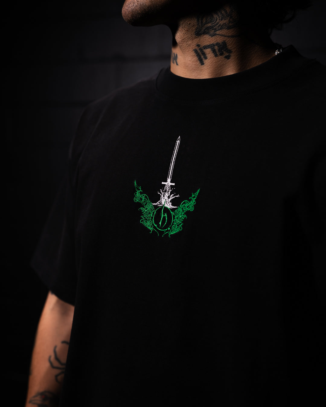 Person wearing a black t-shirt with a green and white graphic design on a dark background