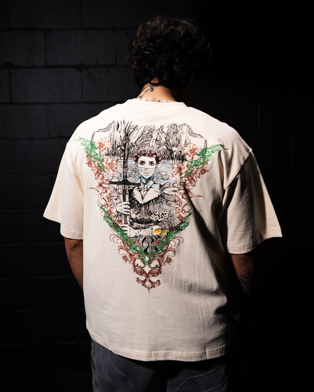 Person wearing a beige t-shirt with a detailed graphic on the back against a dark background