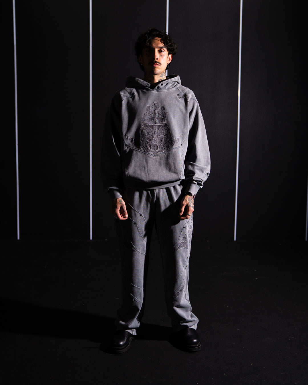 Person wearing a gray hoodie and pants against a dark background