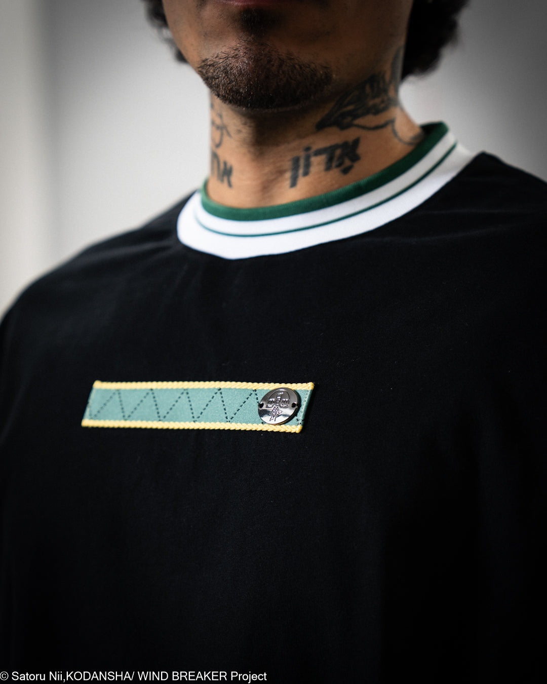 Black t-shirt with a green and white collar and a small patch on the chest.