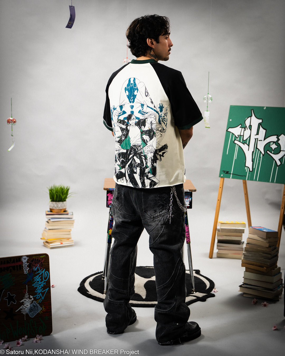 Person wearing a black and white graphic t-shirt in an artistic setting with books and art supplies.