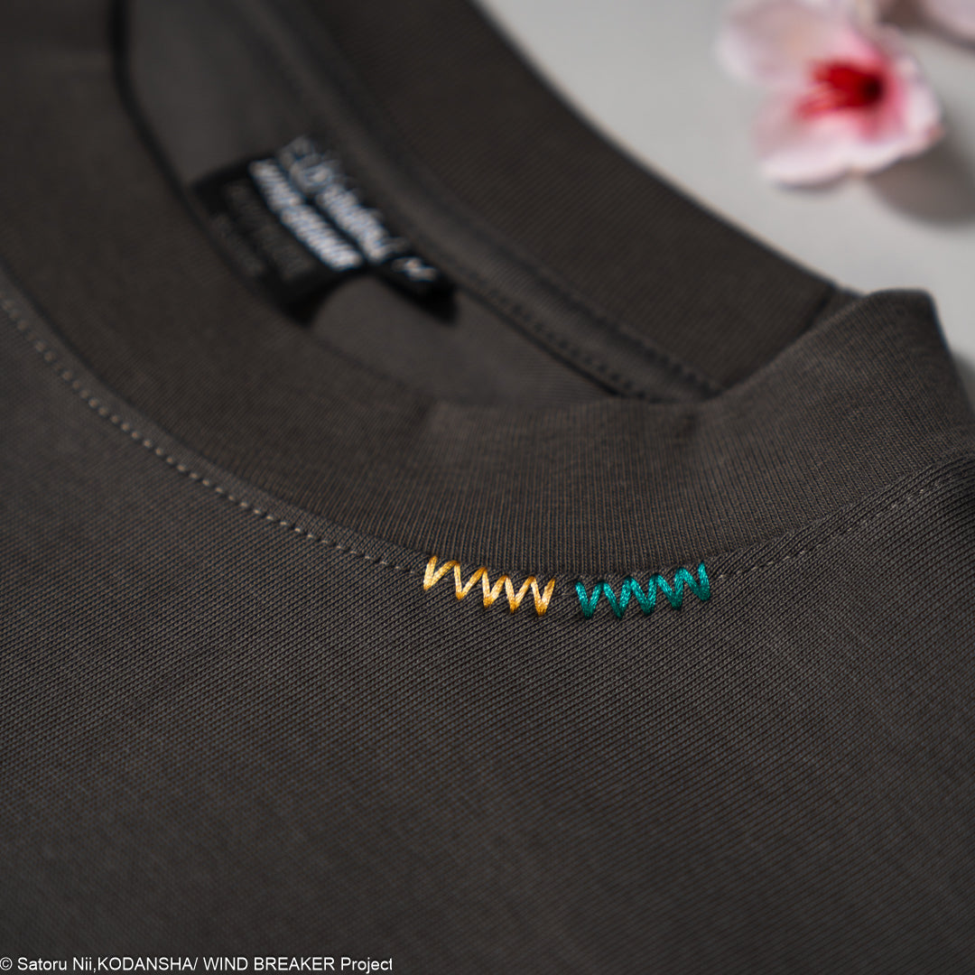 Close-up of a dark gray shirt with colorful embroidered design on a light gray background.