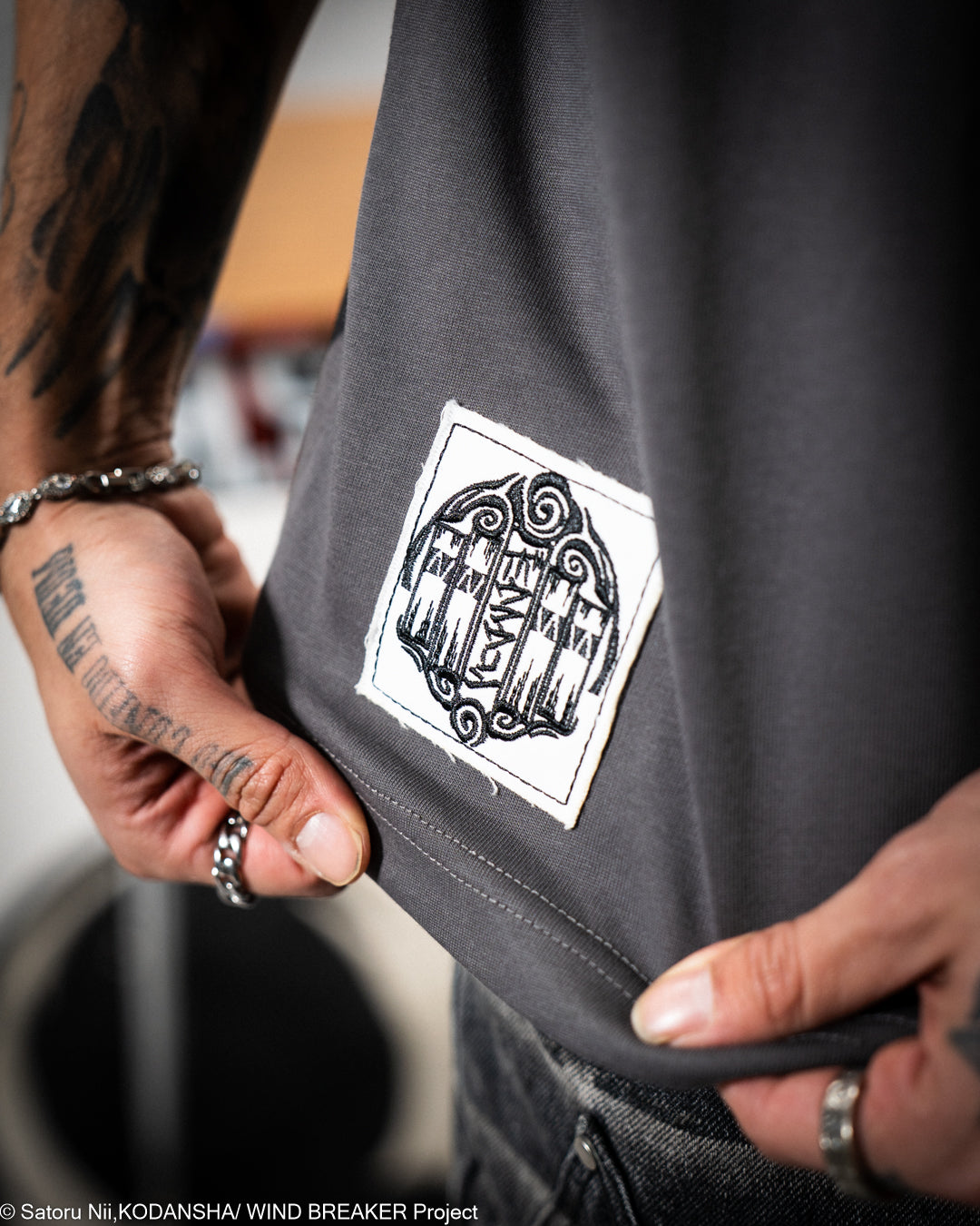 Gray shirt with a black and white sewn patch.