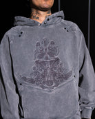 Person wearing a gray hoodie with a detailed design on the chest against a black background