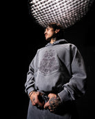 Person wearing a gray hoodie with a graphic design, standing against a black background with studio lighting.