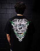Person wearing a black t-shirt with a detailed design on the back against a dark brick wall.