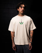 Man wearing a beige t-shirt with a green logo against a black brick wall.