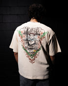 Person wearing a beige t-shirt with a detailed graphic on the back against a dark background