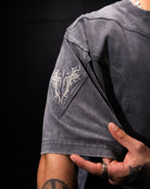 Person wearing a dark gray t-shirt with an embroidered design on the sleeve against a black background