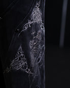 Black garment with intricate white embroidery on a dark background