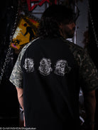 Person wearing a black shirt with character gas mask designs on the back, standing in a dark setting.