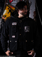 Person wearing a black jacket with patches in a dark setting