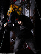 Person wearing a black outfit with red x stitches on hood of jacket against a background.