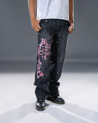Black denim jeans with cherry blossom floral embroidery and armored inspired paneling. 