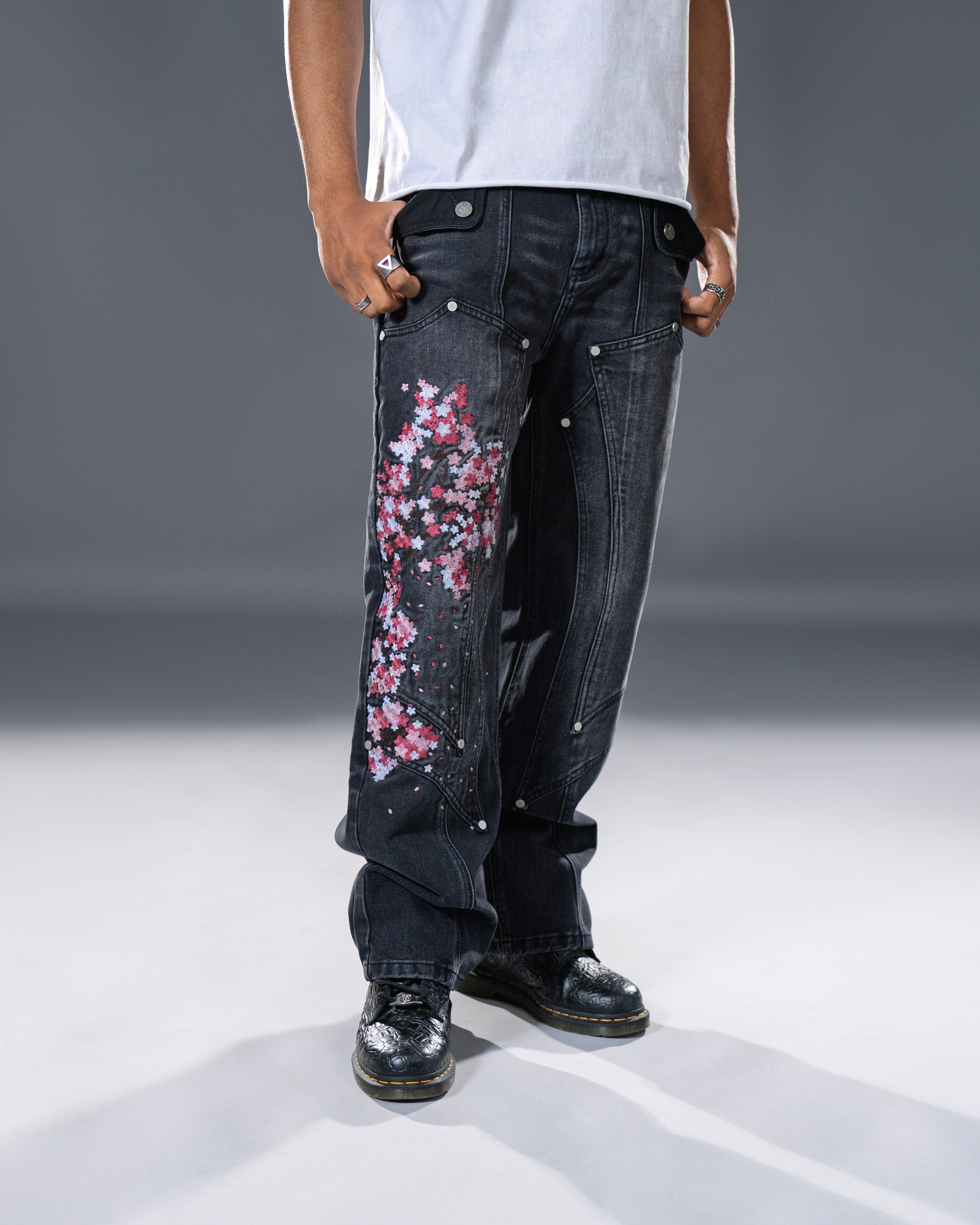 Black denim jeans with cherry blossom floral embroidery and armored inspired paneling. 