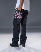 Black denim jeans with cherry blossom floral embroidery and armored inspired paneling. 