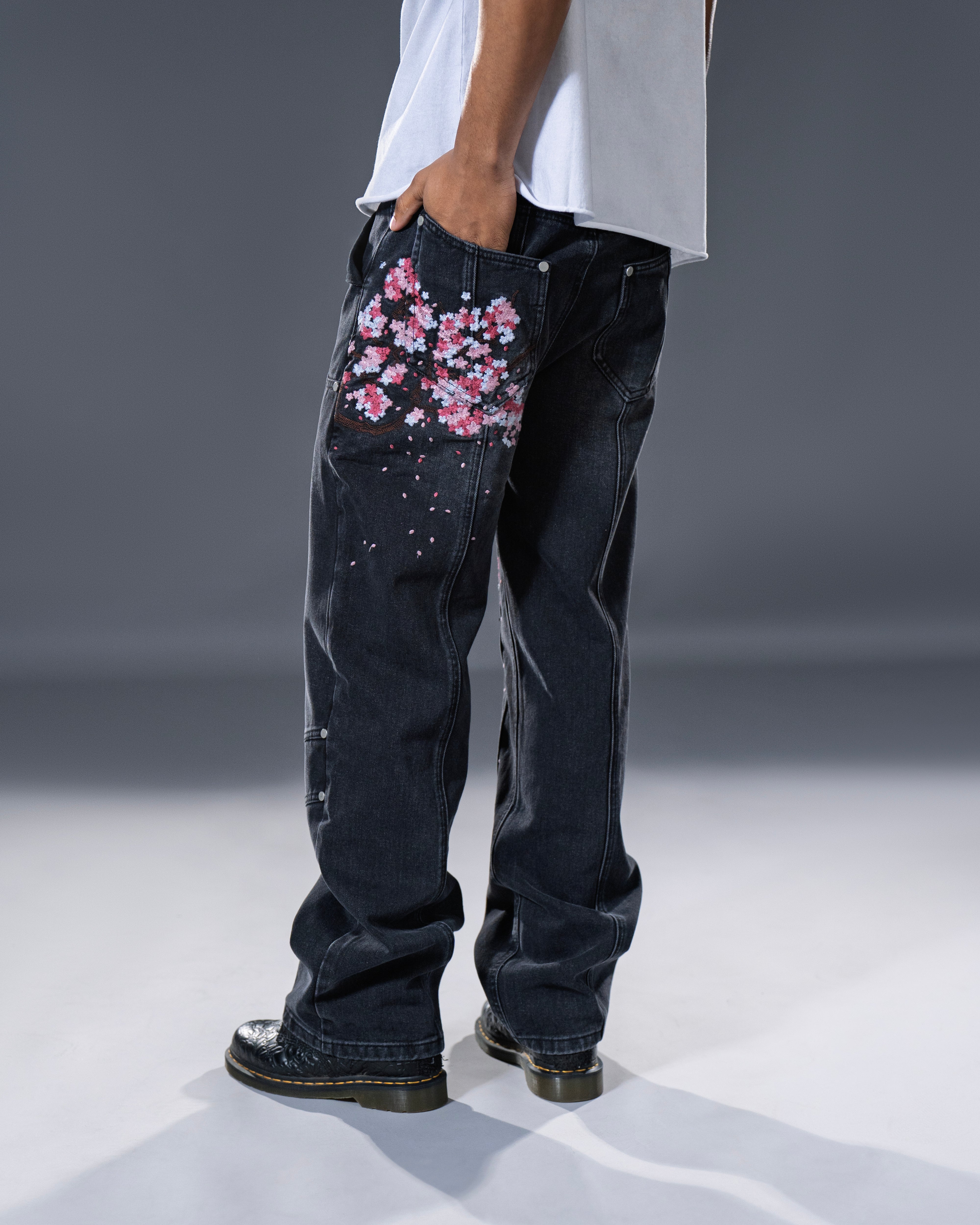 Black denim jeans with cherry blossom floral embroidery and armored inspired paneling. 
