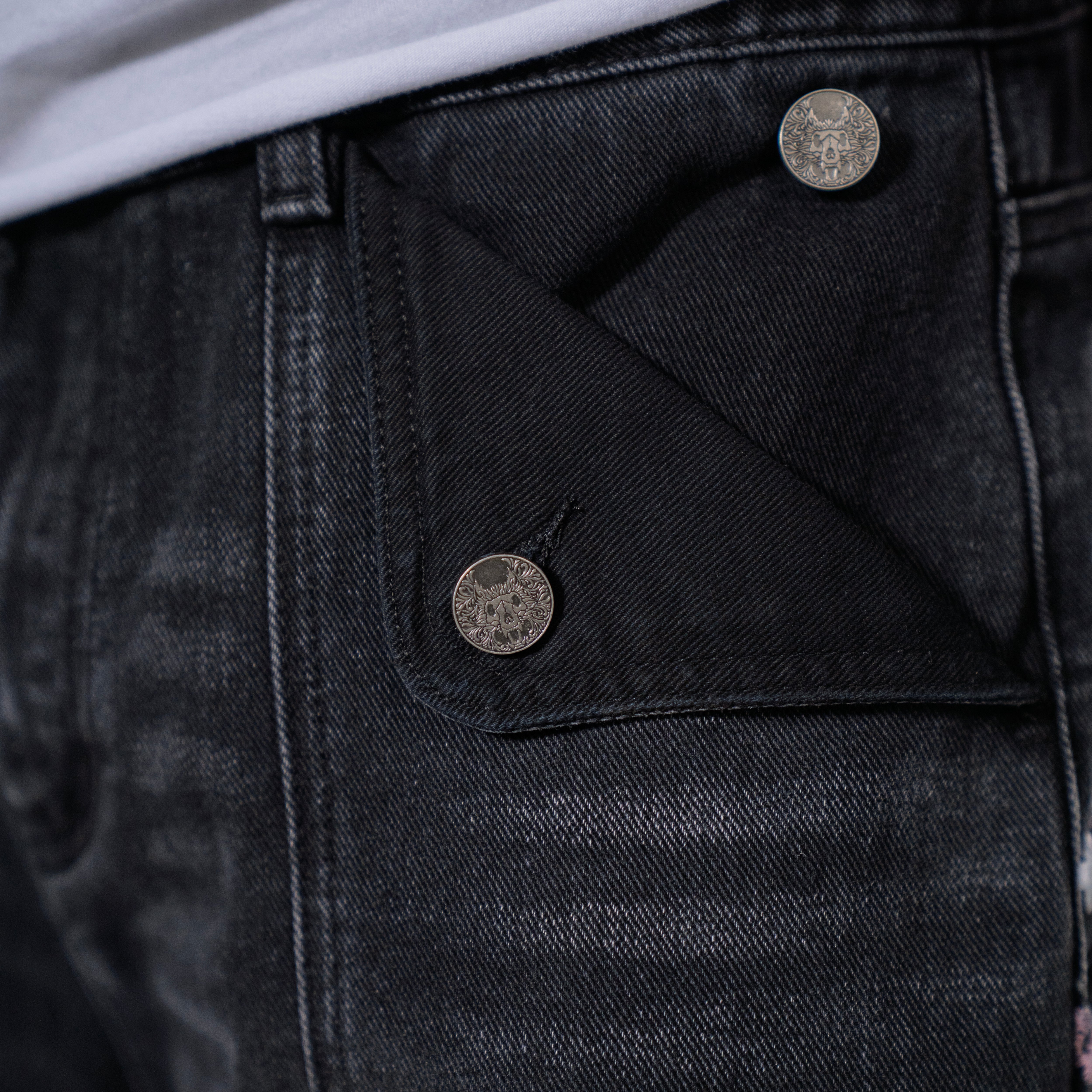 Black denim jeans with cherry blossom floral embroidery and armored inspired paneling. 