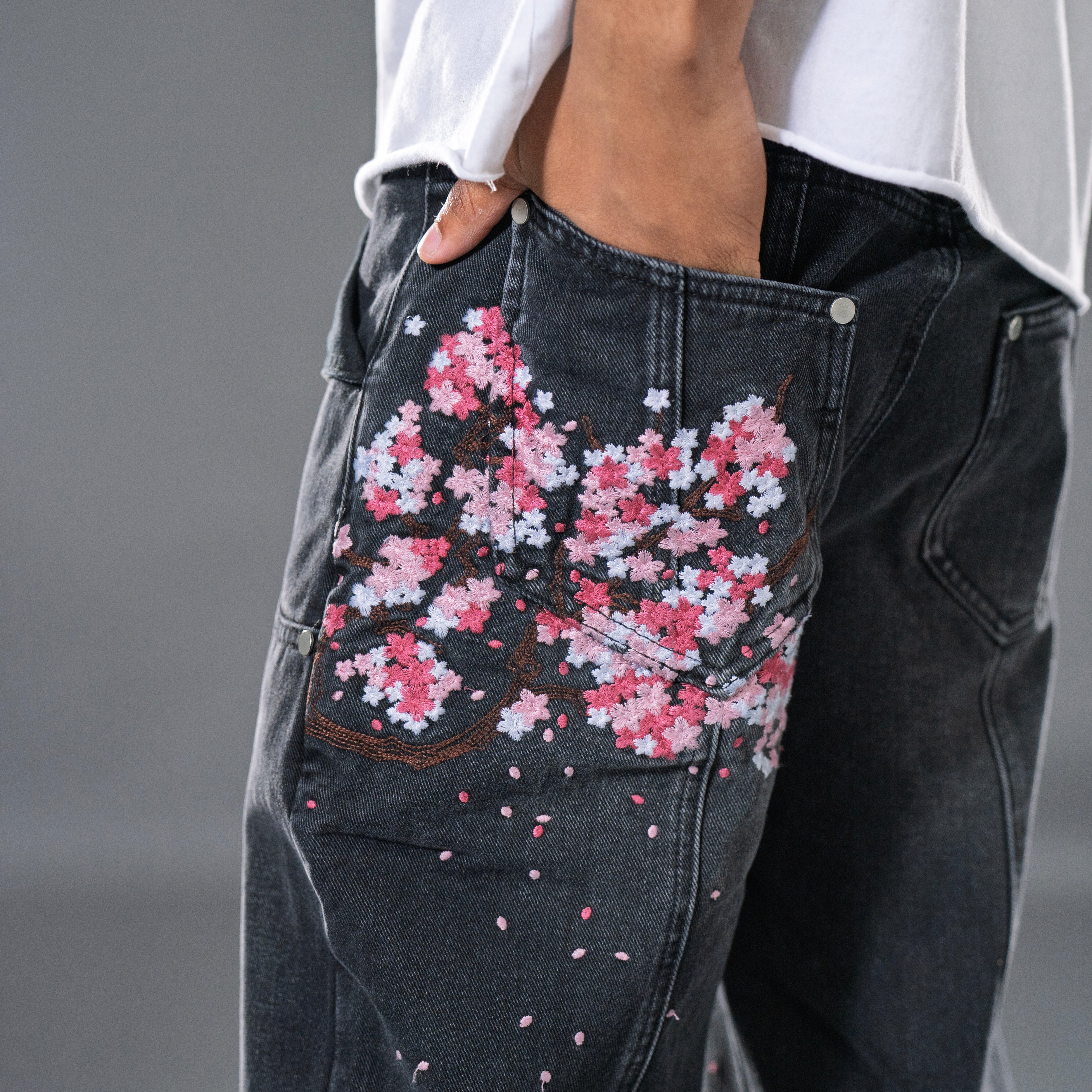 Black denim jeans with cherry blossom floral embroidery and armored inspired paneling. 