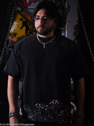 Person wearing a black outfit with decorative elements in a dark setting