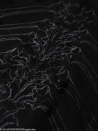 Close-up of black jacket with spine design embroidery on a dark background