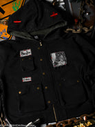 Black jacket with patches and bronze hardware with embroidered details. 