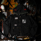Black jacket with patches, red crosses on hood and bronze hardware on a dark background