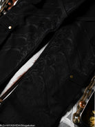 Close-up of a black sweatpants with intricate patterns and hardware buttons.