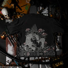 Black t-shirt with a white graphic design of a character sitting among mushrooms on a dark background.