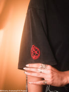 Black shirt with red emblem held by a person wearing rings, against a blurred background.