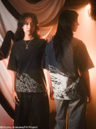 Two people wearing black and dark blue t-shirts in outfits against a warm-toned background.