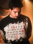 Man wearing a black and white sweater with pixelated design and numbers, against a warm-toned background.