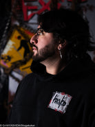 Man wearing glasses and a black hoodie with a logo, standing. 