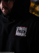 Person wearing a black hoodie with a logo on the chest, blurred background