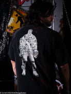 Person wearing a black t-shirt with a white graphic design on the back, standing in a dark room.