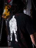 Person wearing a black t-shirt with a white graphic design on the back, standing in a dark room.