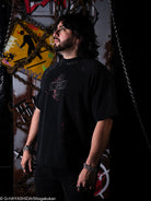 Man wearing a black t-shirt with a logo in a dark, industrial setting