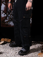 Person wearing black cargo pants and black shoes on a rocky ground with a dark background.