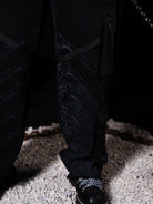 Person wearing black pants with a textured floor on a dark background