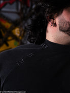 Close-up of a person wearing a black shirt with decorative stitching, blurred background