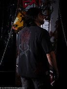 Person wearing a black t-shirt with a red design on the back, standing in a dark room with graffiti on the wall.