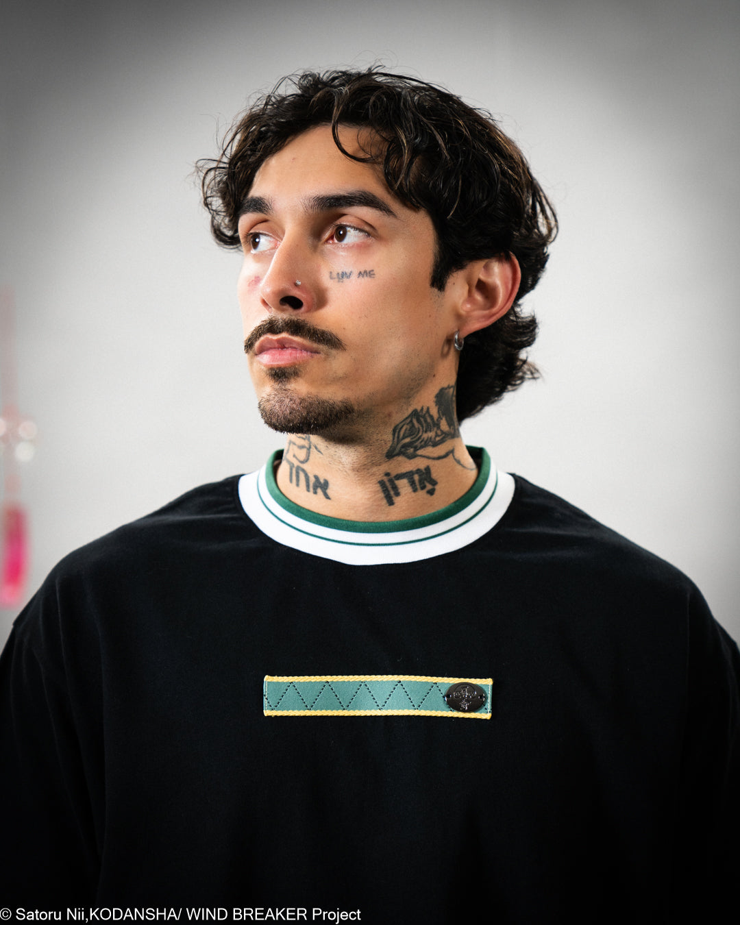 Man with tattoos wearing a black t-shirt with a green and white collar