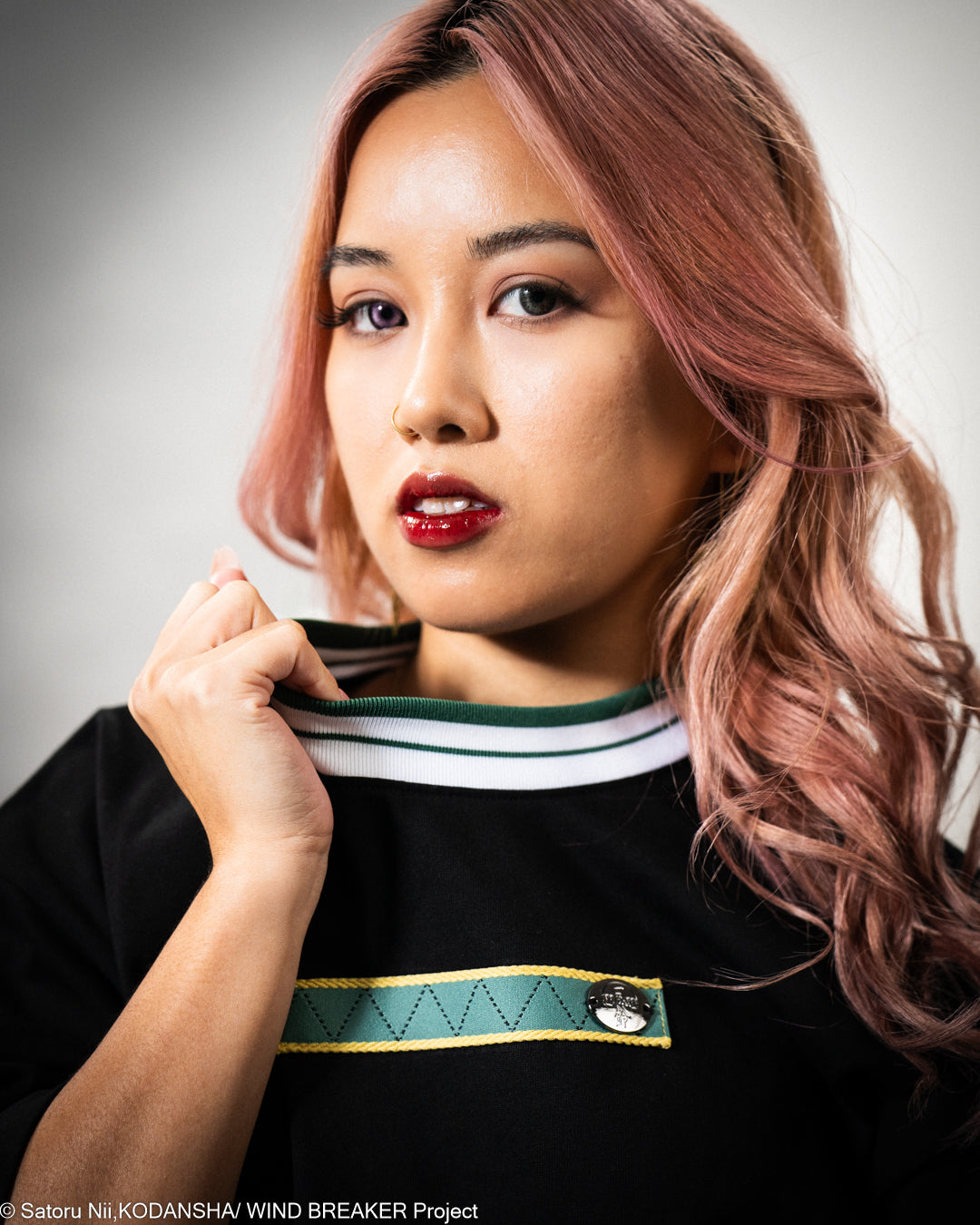 Woman with pink hair wearing a black t-shirt  with green and white accents.