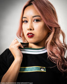 Woman with pink hair wearing a black t-shirt  with green and white accents.