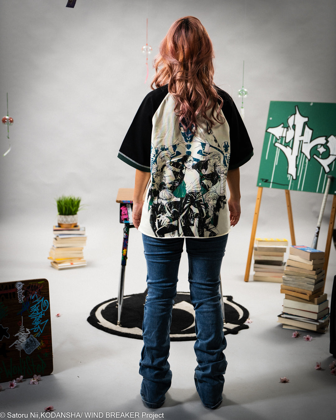 Person wearing a black and white graphic shirt in an indoor setting with books and art supplies.