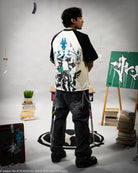 Person wearing a black and white graphic t-shirt in an artistic setting with books and art supplies.