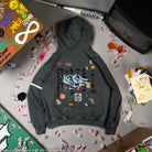 Gray hoodie with colorful designs on a gray surface with various items around