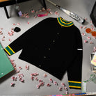 Black knitted jacket with green and yellow accents on a surface with scattered flowers. 