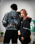 Two people wearing hoodies with intricate designs, standing close together.